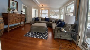 A spacious living room with a wooden floor, a large sectional sofa, a small table, and a cabinet. - Lake Views, steps to Lake! Two story home, professionally decorated! Sleeps 6!  (Delavan Lake)