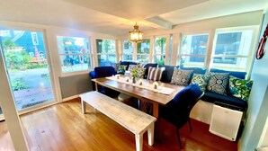 A dining area with a wooden table, benches, and a sofa with patterned cushions. Large windows provide a view of the outdoors. - Lake Views, steps to Lake! Two story home, professionally decorated! Sleeps 6!  (Delavan Lake)