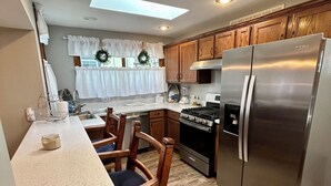 A compact kitchen with wooden cabinets, a stainless steel refrigerator, a dining table with chairs, and a skylight above the sink. - Lake Views, steps to Lake! Two story home, professionally decorated! Sleeps 6!  (Delavan Lake)