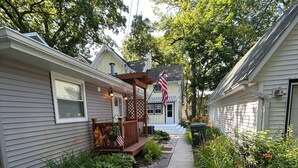 A residential street with houses on either side, a sidewalk, and a small garden area with plants and a wooden deck. - Lake Views, steps to Lake! Two story home, professionally decorated! Sleeps 6!  (Delavan Lake)