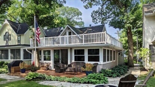 A two-story house with a covered porch, a flag, and outdoor seating. - Lake Views, steps to Lake! Two story home, professionally decorated! Sleeps 6!  (Delavan Lake)
