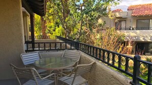Un balcon doté d’une table en verre et de quatre chaises, entouré d’une rambarde noire et de verdure.