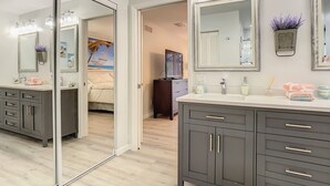 A modern bathroom with a large mirror, a vanity with a sink, and a shower area. - Beautiful Cozy 3-bedroom House (Naples)