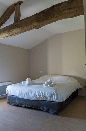 A bedroom with a large bed, wooden beams on the ceiling, and a radiator on the wall.