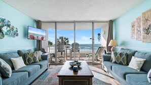 Ein Wohnzimmer mit großem Fenster zum Strand, einer Sofagarnitur, einem Couchtisch und Wanddekoration.