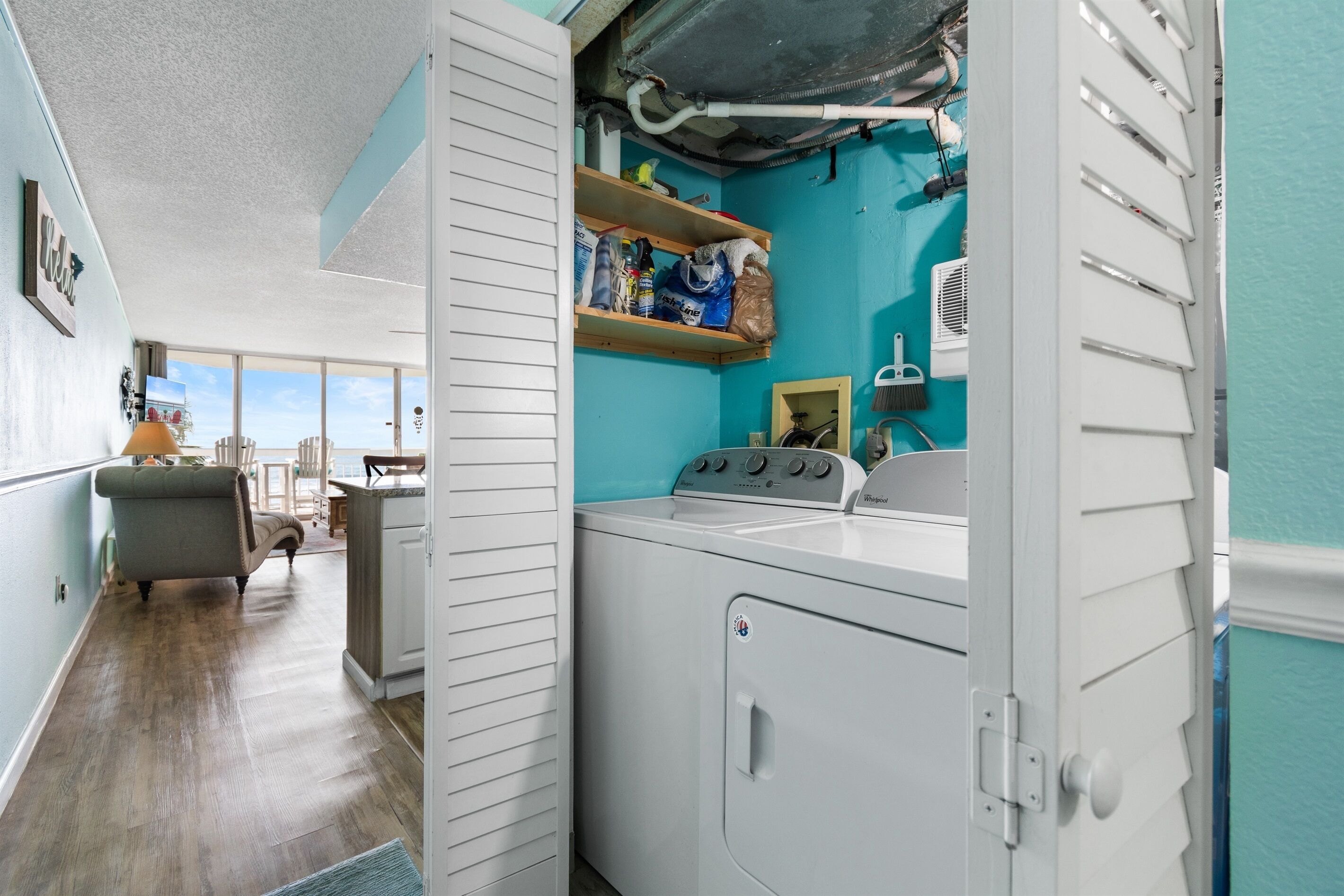 A laundry room with a washing machine, shelves with cleaning supplies, and a view of the outdoors.