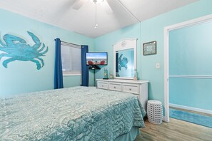 A bedroom with a bed, a dresser, a mirror, and a door. - Garden City Beach Oceanfront Condo 110 | Rising Tides Properties Rental (Murrells Inlet)