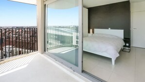 Ein modernes Schlafzimmer mit einem großen Bett, einer Glastür, die auf einen Balkon führt, und Blick auf die Stadt.
