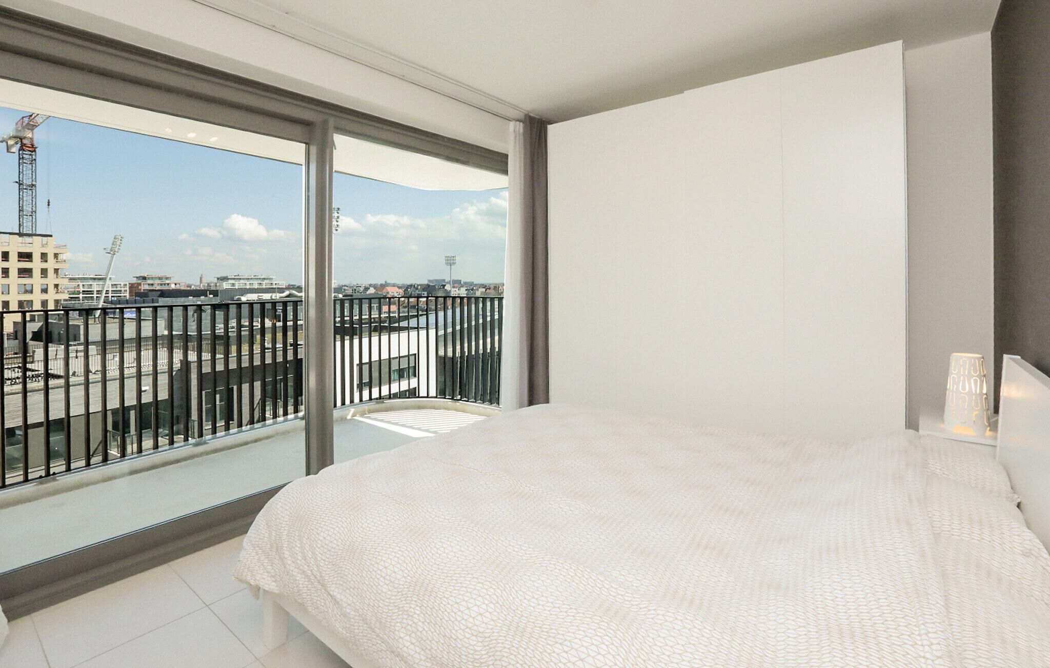 Una habitación de hotel moderna con una cama grande, vistas de la ciudad a través de ventanas de piso a techo y un balcón con barandilla.