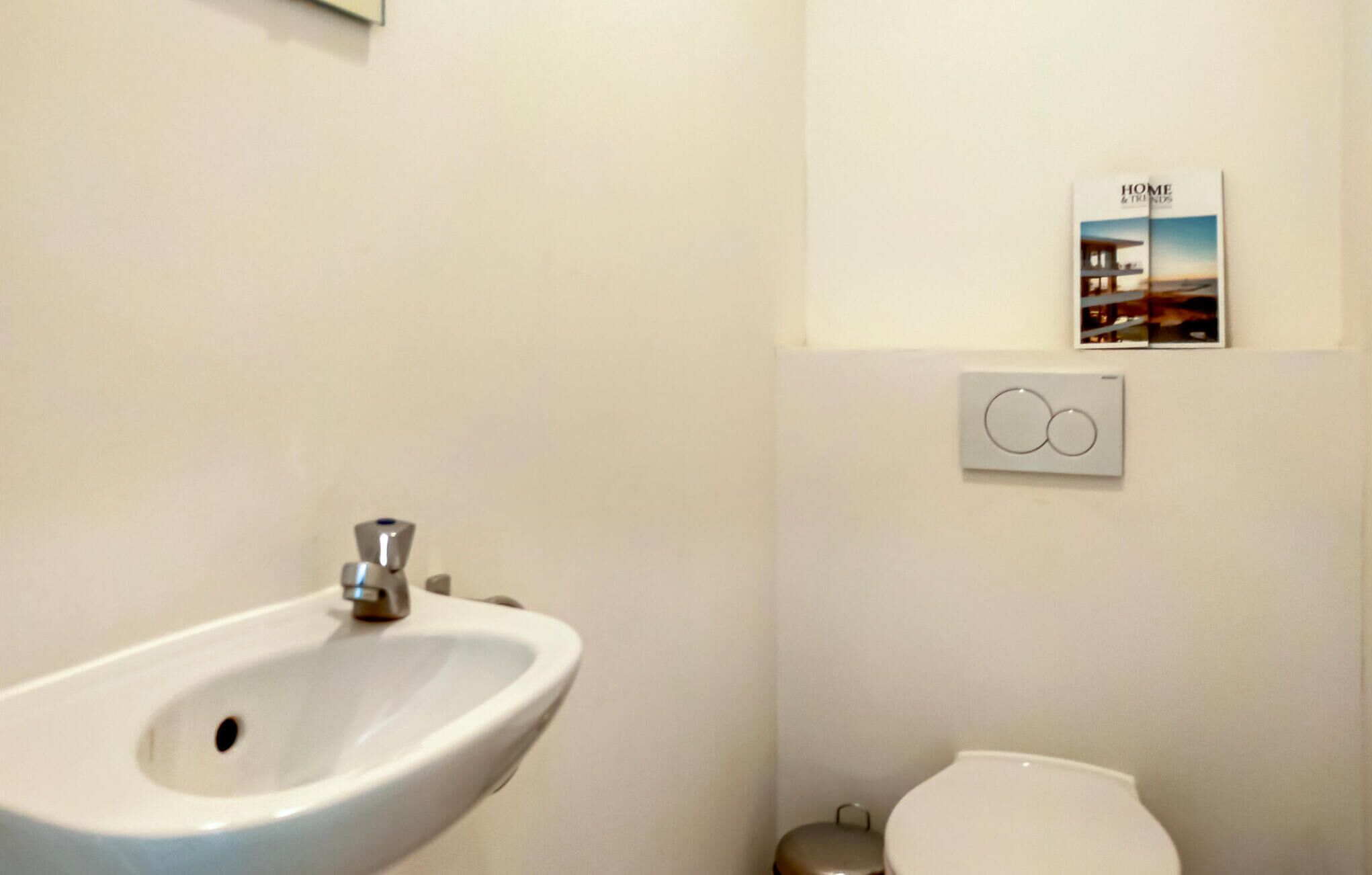 Ein Badezimmer mit einem weißen Waschbecken, einer Toilette und einem Thermostat an der Wand.