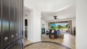 A spacious living area with a stone-tiled floor, a dark-toned sofa, and a ceiling fan.