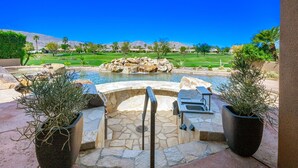 A pool area with a stone deck, a hot tub, and a grill.