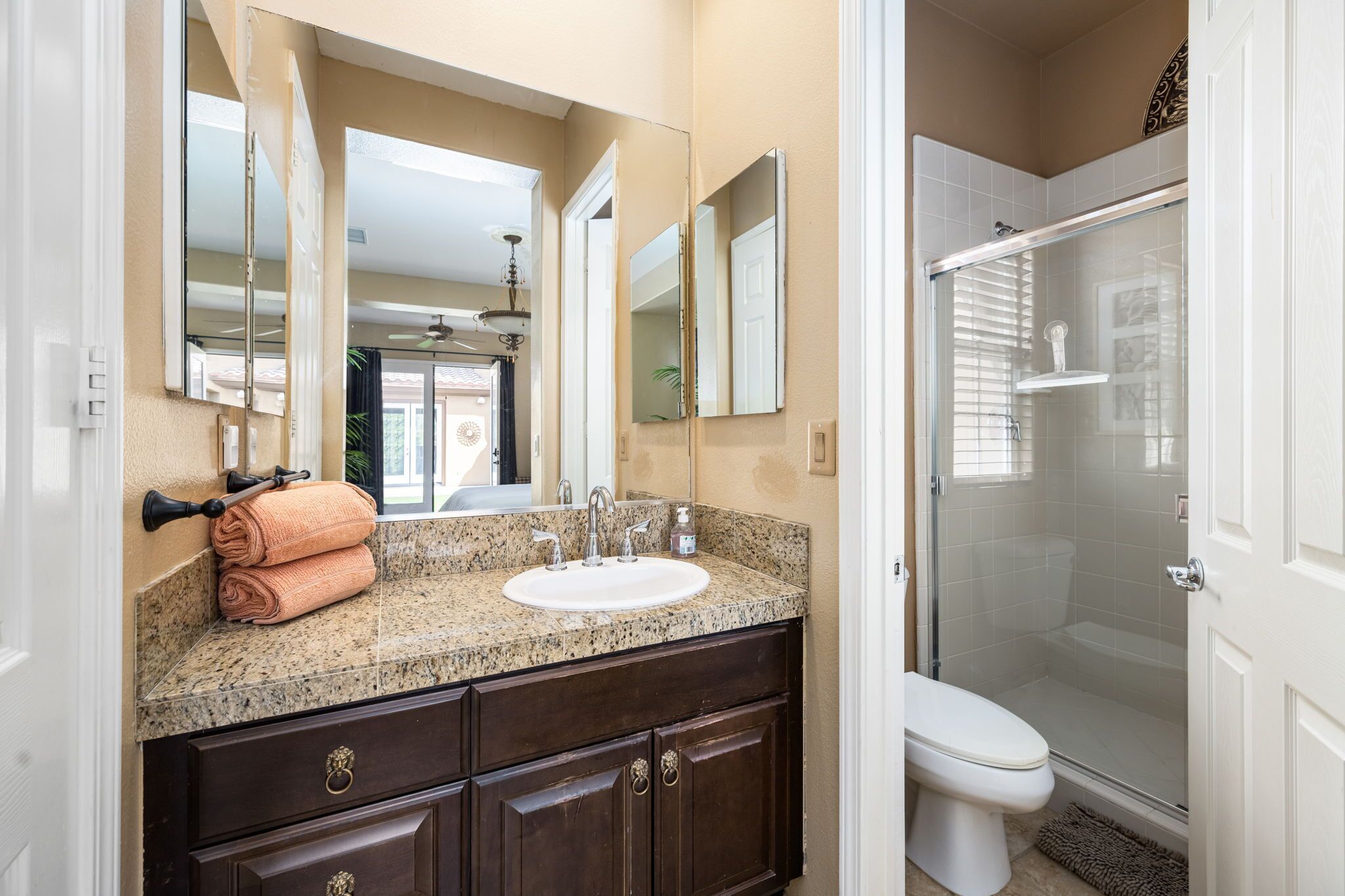 Un bagno con lavabo su piano in granito, mobile contenitore in legno scuro, un ampio specchio e cabina doccia in vetro.