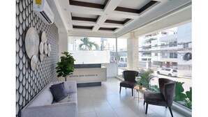 A modern reception area with a white reception desk, grey sofas, and a large window offering a view of the cityscape. - Modern & Cozy place w/pool & Parking in Downtown (Santo Domingo)