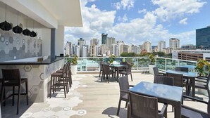 A rooftop terrace with a city view, furnished with tables and chairs, and a glass railing. - Modern & Cozy place w/pool & Parking in Downtown (Santo Domingo)