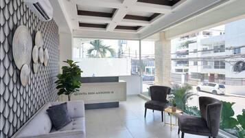 A modern reception area with a white reception desk, grey sofas, and a large window offering a view of the cityscape.