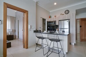 A modern kitchen with a central island, bar stools, a microwave, a refrigerator, and a clock on the wall.