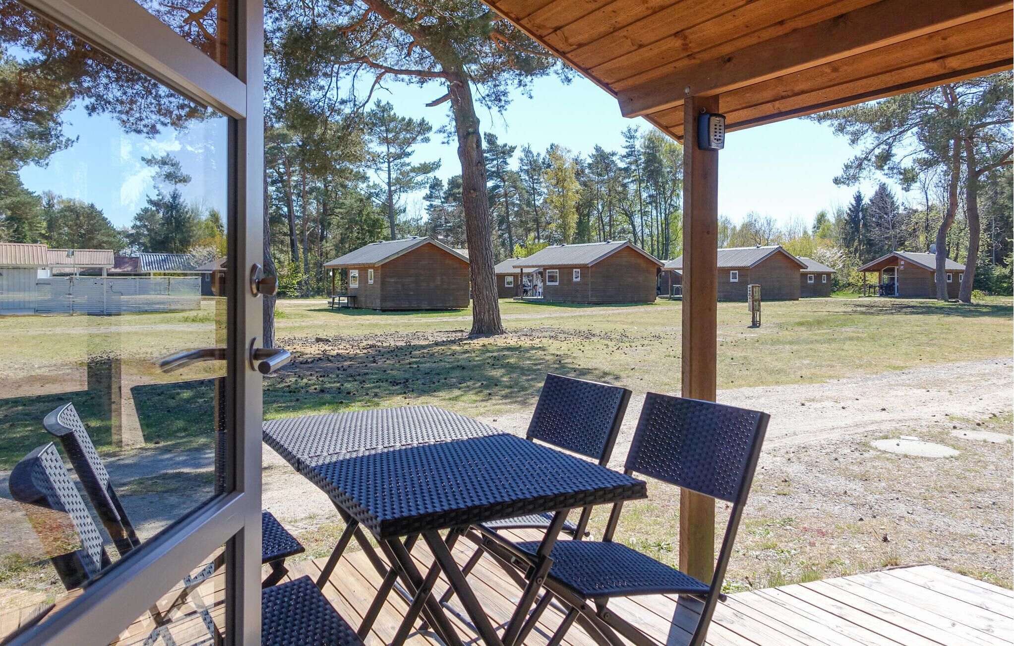 A covered outdoor seating area with metal tables and chairs, overlooking a campground with wooden cabins.