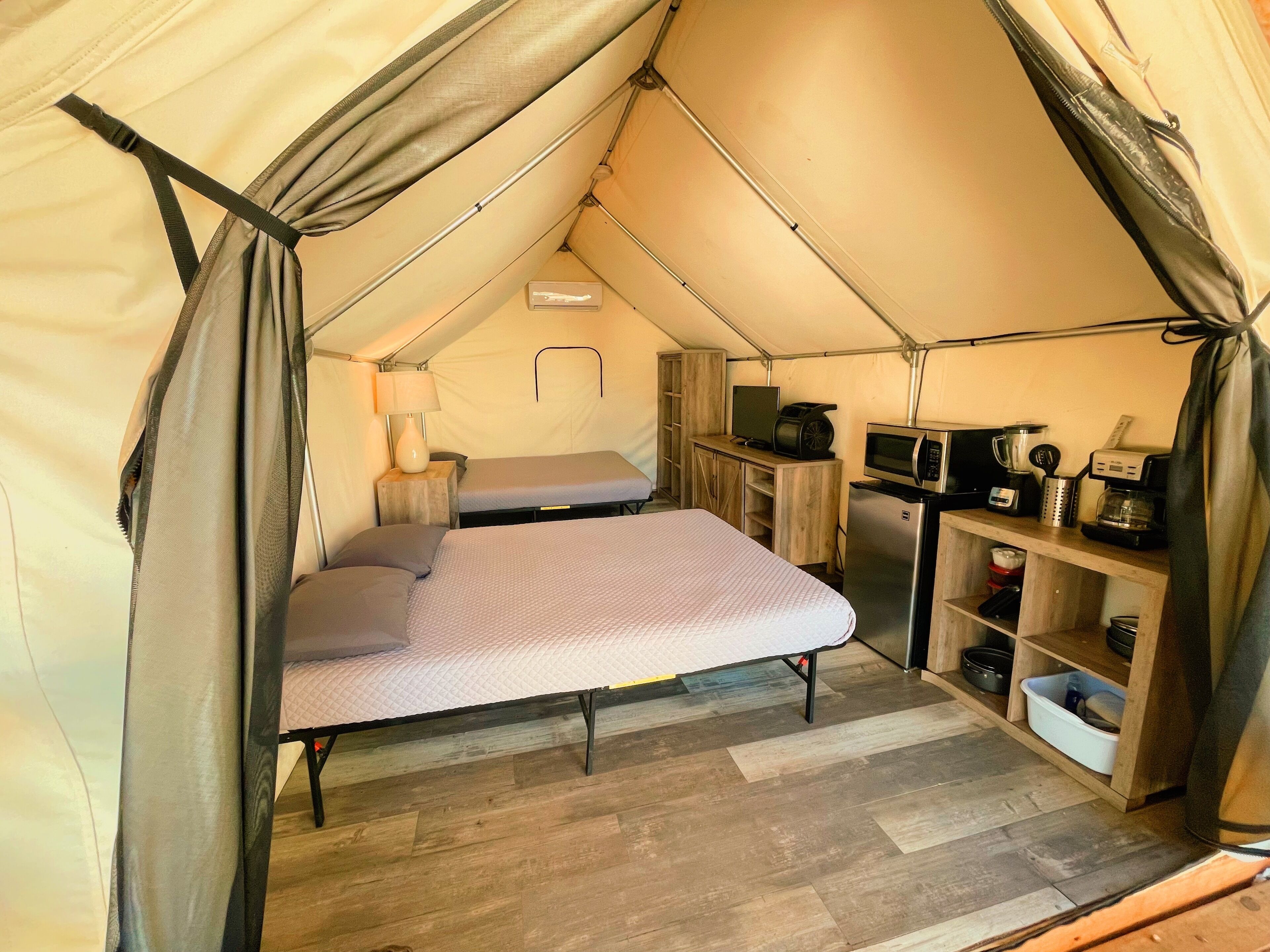 A tent with a bed, a small desk, a microwave, and a coffee maker.