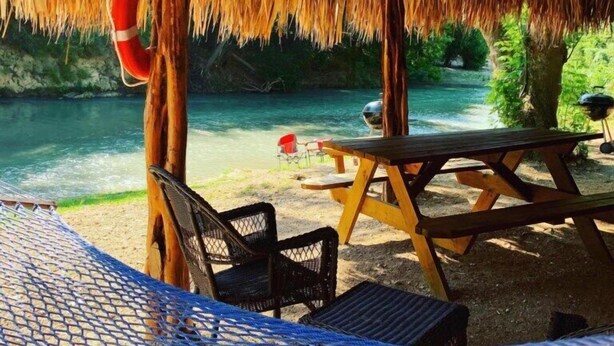 A beachside picnic area with a thatched roof, a hammock, and a picnic table.