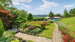 A landscaped garden with a stone pathway leading to a pool area, surrounded by various plants and trees.