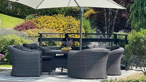 An outdoor patio with a wicker sofa set, a table with a bowl of fruit, and a pergola with yellow flowers.