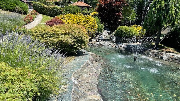 A clear water feature with a waterfall, surrounded by well-maintained gardens and a pathway.