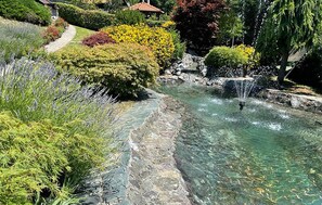 Un bassin d’eau claire agrémenté d’une cascade, entouré de jardins bien entretenus et d’un sentier.