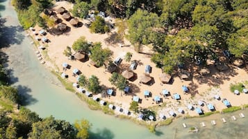 An aerial view of a beach resort with thatched-roof huts and sun loungers arranged in rows along the shoreline.