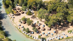 An aerial view of a beach resort with thatched-roof huts and sun loungers arranged in rows along the shoreline.
