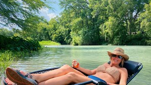 Iemand ligt ontspannen in een stoel aan een rivier, met een drankje in de hand.