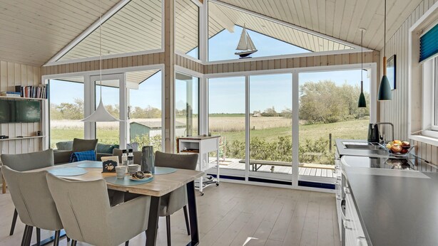 A spacious kitchen with large windows, a dining area with a table and chairs, and a view of the countryside.