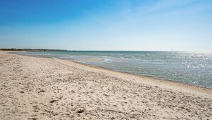 A wide sandy beach with gentle waves, a clear blue sky, and a distant pier.