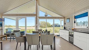 A spacious kitchen with large windows, a dining area with chairs, and a view of the countryside.