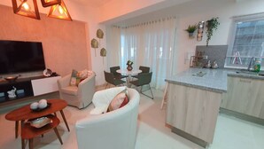 Ein modernes Wohnzimmer mit einem Flachbildfernseher, einem Essbereich mit rundem Tisch und Stühlen sowie einer Küche mit Granitabdeckung und einem Fenster.