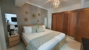 Ein Schlafzimmer mit Bett, Nachttischen, einem Spiegel, einem Fernseher, einer Chandelier und Holzschränken.