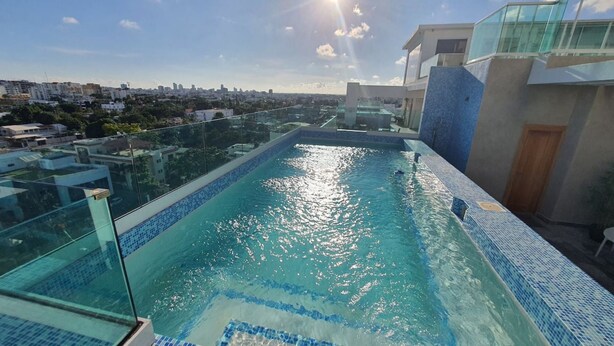 Ein Dachpool mit klarem, blauem Wasser, umgeben von Glasgeländern und Blick auf die Stadt.