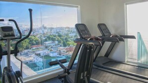 Ein Fitnessstudio mit Laufbändern und einem Crosstrainer, große Fenster mit Blick auf die Stadt.