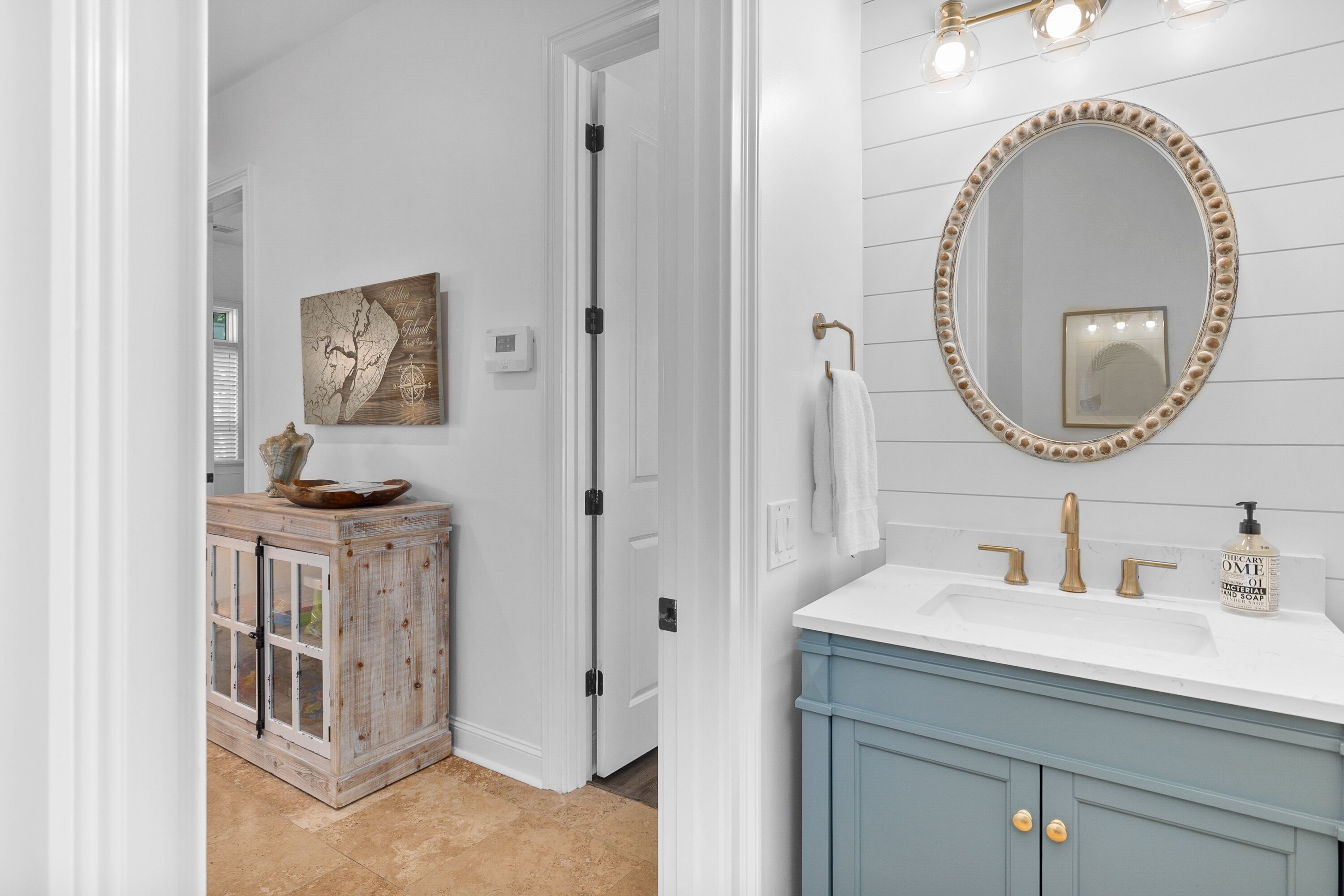 A bathroom with a white vanity, a round mirror with a decorative frame, and a wall-mounted light fixture.