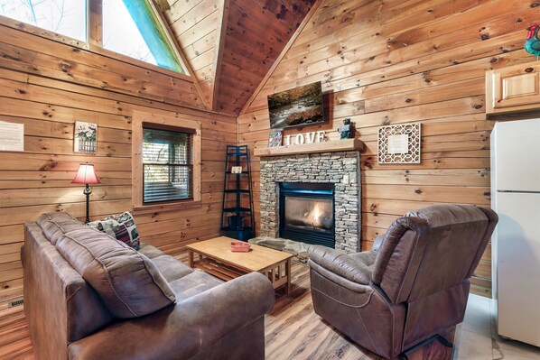 A cozy cabin interior with a stone fireplace, leather sofas, and wooden walls.