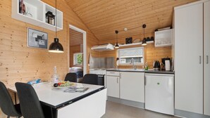 A modern kitchen with white cabinets, a dining table with chairs, and a window overlooking greenery. - Beautiful home in Nexø with kitchen (Nexø)