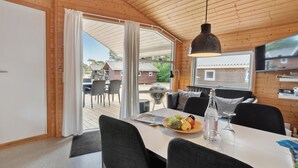 A wooden-paneled room with a dining table, chairs, a TV, and a view of the outside. - Beautiful home in Nexø with kitchen (Nexø)