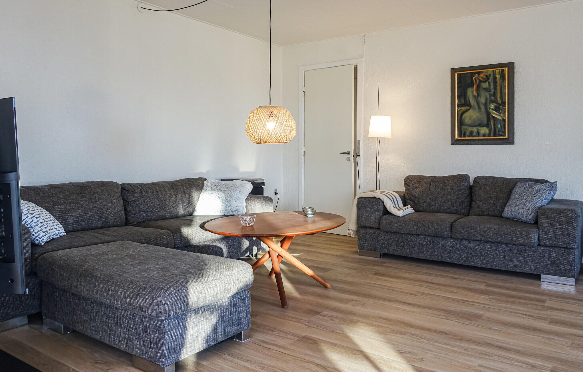 Una sala de estar con dos sofás grises, una mesa de centro de madera, una lámpara de techo tejida y un cuadro en la pared.