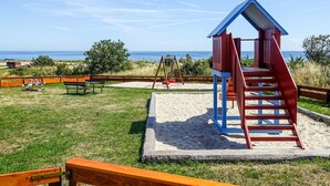 A beach playground with a slide, swings, and a bench.