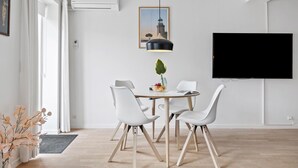 Et moderne spiseområde med et rundt bord, hvide stole, en pendellampe og et fladskærms-tv monteret på væggen.