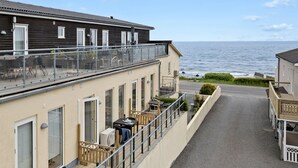 En bygning ved havet med balkon, lille udendørs siddeområde og udsigt over havet.