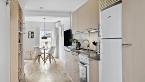 Et moderne køkken med træskabe, en stålvask og en indbygget ovn. Der er et spiseområde med et bord og stole, samt udsigt udendørs gennem et vindue.