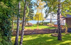 A serene garden with a wooden fence, a small shed, and a view of a lake. - Awesome home in Boruja with lake view (Boruja)