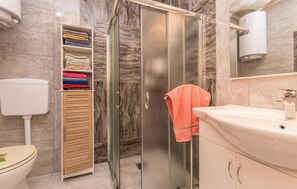 A bathroom with a glass shower enclosure, a toilet, a sink, and a towel rack with towels.