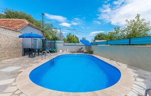 A swimming pool with a stone deck, surrounded by a low wall, and shaded by blue umbrellas.